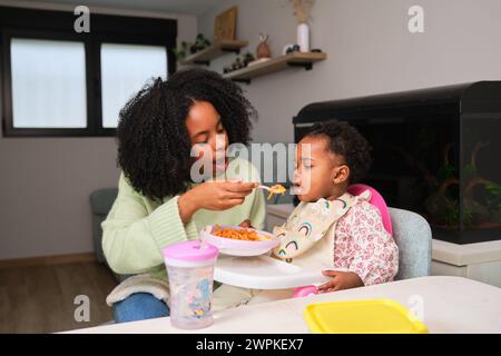 Madre cubana che dà da mangiare agli spaghetti con salsicce alla figlia. Foto Stock