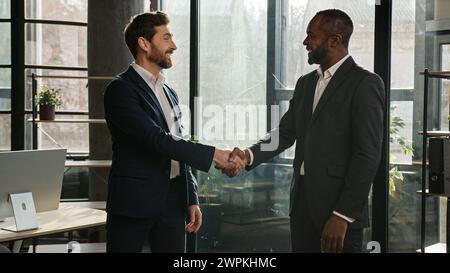 Due uomini diversi uomini d'affari multirazziali che parlano in carica si stringono la mano dopo il successo dei negoziati. Venditore uomo caucasico stretta di mano afroamericano Foto Stock