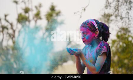 Giovane ragazza allegra e simpatica con polvere di colori holi applicata che mostra mani colorate alla macchina fotografica durante la celebrazione del festival holi Foto Stock