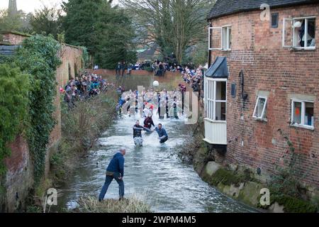 08/02/16 i giocatori inseguono il pallone attraverso Henmore Brook mentre la partita di calcio del Royal Shrovetide viene giocata attraverso la città di Ashbourne, Derbyshire. U' Foto Stock