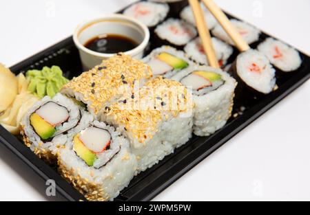 Primo piano di sushi per andare in una scatola da asporto nera con bacchette di legno su sfondo bianco Foto Stock