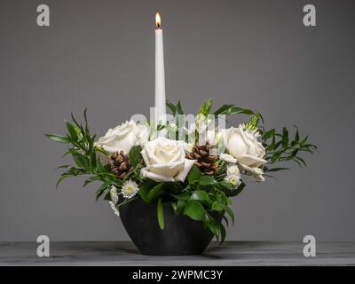 Disposizione dei tavoli floreali con rose bianche e mini crisantemi, fogliame e coni di abete, visti su sfondo grigio. Foto Stock