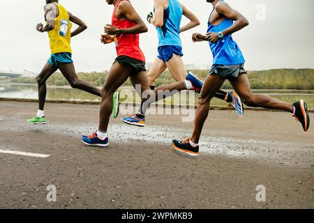 i principali corridori di gruppo vestiti con abiti sportivi brillanti corrono lungo il fiume calmo, maratona estiva Foto Stock