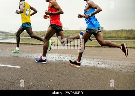 i principali corridori africani vestiti con abiti sportivi brillanti corrono lungo il fiume calmo, maratona estiva Foto Stock