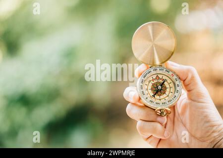 Sullo sfondo di una foresta serena e di un lago tranquillo, la mano di una donna afferra saldamente una bussola Foto Stock