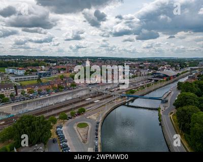 Questa fotografia aerea di Halle rivela l'intricato collegamento tra i corsi d'acqua della città e le sue infrastrutture. Il fiume che scorre, contornato da sentieri e vegetazione, funge da arteria naturale, mentre i ponti fungono da collegamenti vitali, facilitando il movimento e collegando le comunità. La giustapposizione di movimento e quiete è evidente quando auto e pedoni attraversano i ponti sopra e l'acqua scorre tranquillamente sotto. Sullo sfondo, la città si snoda con una miscela di aree residenziali e commerciali, annidate sotto un cielo spettacolare di nuvole fluttuanti. Questa immagine cattura l'essenza dell'urba di Halle Foto Stock