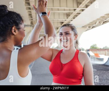Due donne più grandi ne danno cinque dopo un intenso allenamento. Una donna sorridente e di grandi dimensioni che ne dà cinque al suo compagno di fitness. Foto Stock