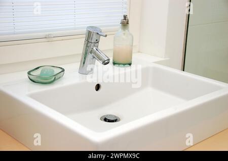 I moderni interni del bagno presentano un elegante lavandino bianco, un elegante rubinetto e saponi ordinati, creando un design pulito e minimalista Foto Stock