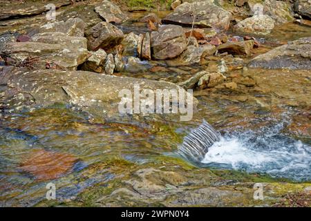 Una vista ravvicinata dell'acqua cristallina che scorre a valle sopra e intorno alle rocce colorate del torrente Foto Stock