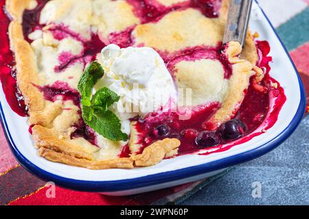 Ciotola di frutti di bosco in teglia smaltata, guarnita con gelato, decorazione natalizia su sfondo, orizzontale, primo piano Foto Stock