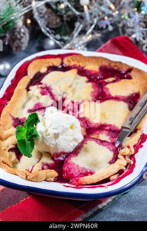 Delizioso ciabattino di frutti di bosco in teglia smaltata, guarnito con gelato, decorazione natalizia su sfondo, verticale Foto Stock