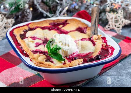 Ciabattino di frutti di bosco fatto in casa in teglia smaltata, guarnito con gelato, decorazione natalizia su sfondo, orizzontale Foto Stock