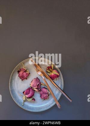 Natura morta con petali di rosa secchi e posate su un piatto di ceramica per San Valentino come segno d'amore Foto Stock