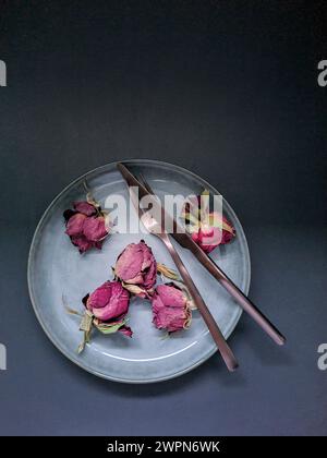 Natura morta con petali di rosa secchi e posate su un piatto di ceramica per San Valentino come segno d'amore Foto Stock
