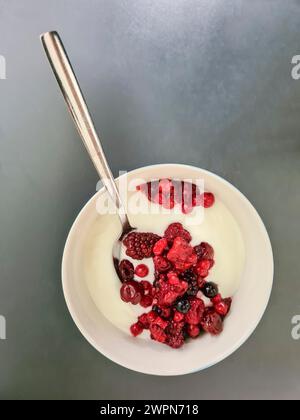 Bacche rosse fresche con yogurt naturale in un recipiente bianco per colazione Foto Stock