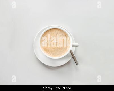 Una tazza di caffè con un piattino bianco e un cucchiaio su una superficie bianca Foto Stock