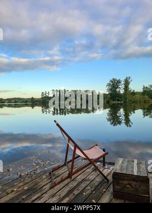 Una sedia a sdraio si erge su una piattaforma di legno sulla riva del lago, vista dell'acqua e del cielo con nuvole, Wannsee, Berlino, Germania Foto Stock