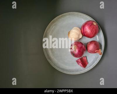 Natura morta con aglio e cipolle rosse su un piatto di ceramica Foto Stock