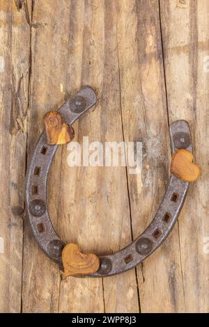 Vecchio ferro di cavallo con 3 cuori di legno su uno sfondo di legno come decorazione, simbolo di felicità Foto Stock