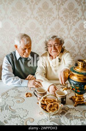 Anziani anziani anziani coppia d'amore romantico bevendo tè con biscotti di samovar. Vecchio pensionato donna insieme. Moglie di un marito anziano in una casa accogliente. Sbirciatina anziana Foto Stock