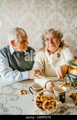 Anziani anziani anziani coppia d'amore romantico bevendo tè con biscotti di samovar. Vecchio pensionato donna insieme. Moglie di un marito anziano in una casa accogliente. Sbirciatina anziana Foto Stock