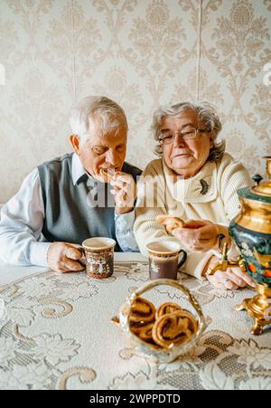 Anziani anziani anziani coppia d'amore romantico bevendo tè con biscotti di samovar. Vecchio pensionato donna insieme. Moglie di un marito anziano in una casa accogliente. Sbirciatina anziana Foto Stock