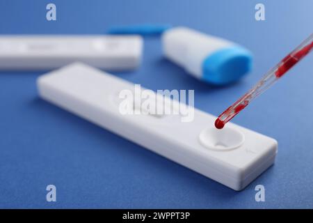 Gocciolamento del campione di sangue su una cassetta per test Express monouso con pipetta su sfondo blu, primo piano Foto Stock