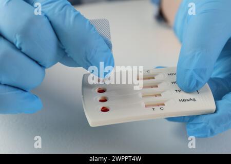 Medico che rilascia la soluzione tampone sulla cassetta per test multi-infezione Express monouso in un tavolo bianco, primo piano Foto Stock