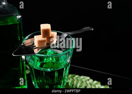 Absinthe in vetro, zucchero di canna e cucchiaio sul tavolo su sfondo nero, spazio per il testo. Bevanda alcolica Foto Stock