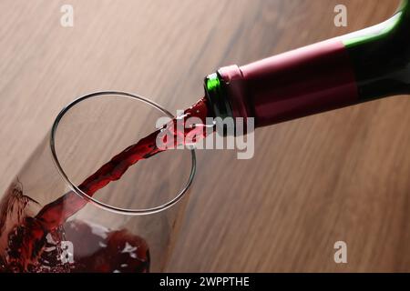 Versare un gustoso vino rosso in bicchiere al tavolo di legno, primo piano Foto Stock