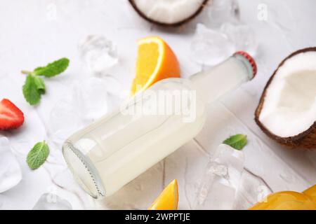 Gustoso kombucha in bottiglia di vetro, frutta fresca e ghiaccio su tavolo bianco, primo piano Foto Stock