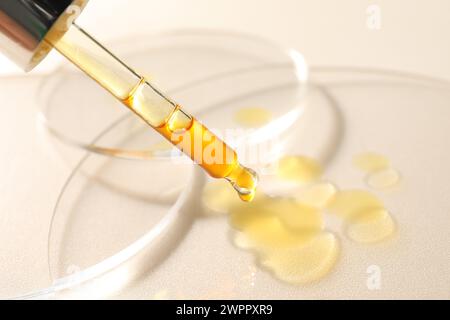 Gocciolamento di siero idratante dalla pipetta su sfondo beige, primo piano Foto Stock