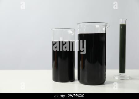 Becher e provetta con olio grezzo nero su tabella bianca, spazio per testo Foto Stock