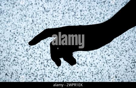 Il contorno scuro di una persona tesa con la mano e il dito puntato si contrasta con lo sfondo luminoso e testurizzato di uno schermo TV con noi bianco Foto Stock