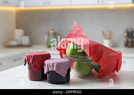 Barattoli di marmellate e mele nel recipiente ricoperti di cera d'api avvolti su un tavolo bianco all'interno Foto Stock