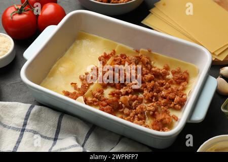 Cottura delle lasagne. Fogli di pasta, carne macinata nel vassoio da forno e pomodoro sul tavolo, primo piano Foto Stock