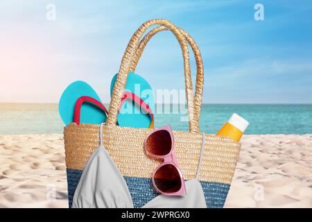 Elegante borsa e altri accessori da spiaggia sulla sabbia vicino al mare Foto Stock