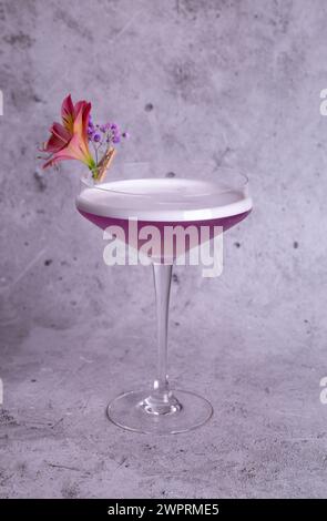 Elegante immagine di un cocktail rosa in un bicchiere con decorazione floreale su sfondo grigio, trasuda classe e raffinatezza. Foto Stock