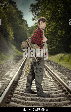 Avventuriero con l'haversack retrò che vagava nella natura sulla ferrovia Foto Stock