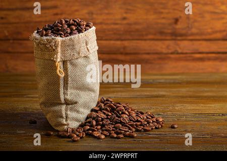 Un sacco di burlap pieno di chicchi di caffè poggiati su un rustico tavolo di legno. Foto Stock