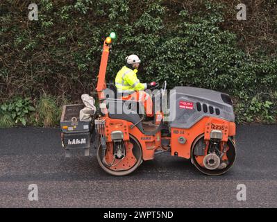 Un lavoratore che guida un compattatore a rulli durante i lavori di ripavimentazione stradale, Regno Unito Foto Stock