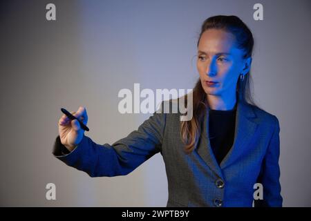 Donna d'affari con una matita leggera in mano destra su sfondo grigio. Concentrati sul volto. Primo piano. Correzione del colore blu. Foto Stock