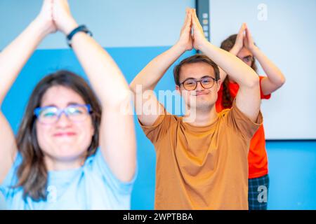 Gruppo felice di disabili che alzano le braccia praticando yoga in palestra Foto Stock