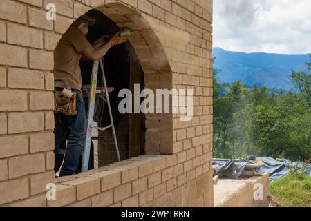 Un falegname su una scala a gradini che smeriglia una struttura in mattoni di adobe per ospitare una finestra, in un cantiere vicino alla città coloniale di Villa de Leyva. Foto Stock