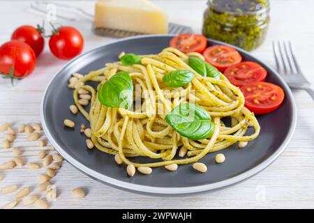 Pesto di pasta, spaghetti con salsa al pesto e foglie di basilico fresco in piatto nero su sfondo bianco di legno servito con ingredienti alimentari. ita tradizionale Foto Stock