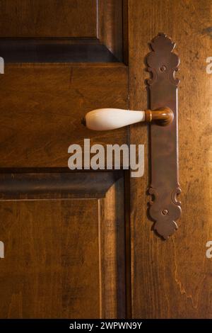 Antica maniglia per porta in porcellana bianca su una vecchia porta in legno nella camera da letto principale al piano superiore all'interno della casa in legno. Foto Stock