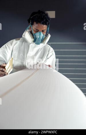 Produzione di tavole da surf, Shaper che lavora sui dettagli della tavola. Concetto di produzione industriale, professionale qualificata, professione e occupazione. Foto Stock