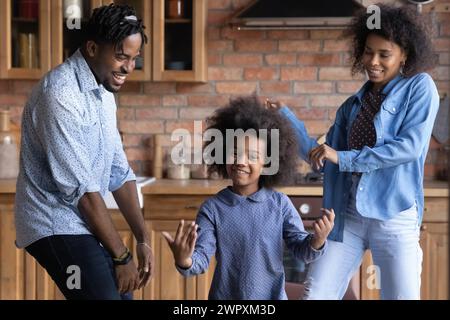 Allegra e vivace coppia africana e figlia che ballano in cucina Foto Stock