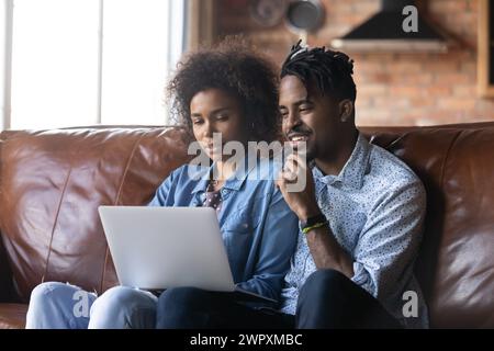 Una coppia africana si siede sul divano con un computer wireless che acquista online Foto Stock