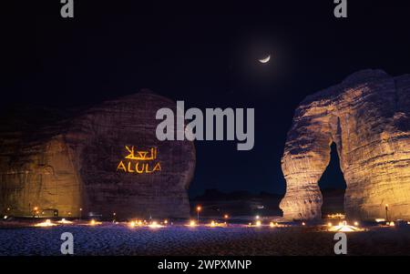 Jabal AlFil - Elephant Rock in serata, paesaggio illuminato, testo Alula e traduzione araba proiettati su sedili a parete in pietra per le persone allestite in Foto Stock